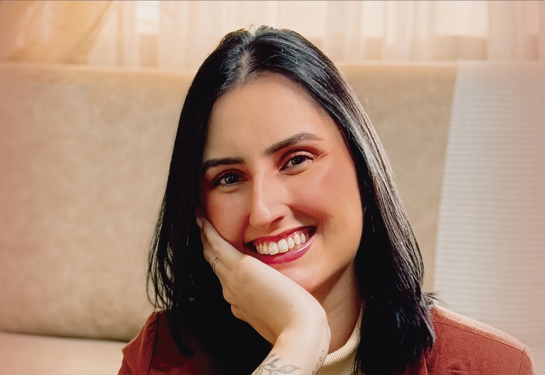 Eduarda Altenhofer sorrindo, com a mão apoiada no rosto, sentada no sofá